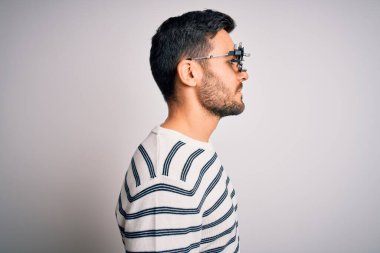 Sakallı, optometri gözlüğü takan, beyaz bir arka planı olan, kendine güveni tam, rahat bir görünüm takınan genç yakışıklı bir adam..