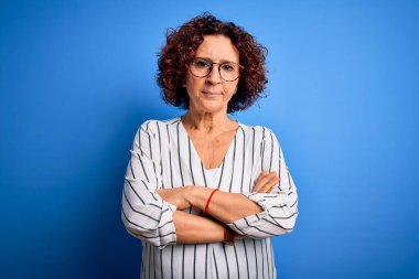 Orta yaşlı güzel kıvırcık saçlı kadın izole edilmiş arka plan şüphecisi ve gergin, kolları çaprazlanmış yüz ifadesini tasvip etmeyen sıradan çizgili gömlek giyiyor. Negatif kişi.