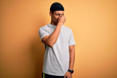 Yakışıklı Afro-Amerikan sporcusu sarı arka planda spor giysisi giyer yorgun burnu ve gözleri ovuşturur yorgun ve baş ağrısı hisseder. Stres ve hüsran kavramı.