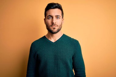 Sakallı, sıradan bir süveter giyen, sarı arka planda duran, yüzünde ciddi bir ifade olan yakışıklı bir genç. Basit ve doğal bir şekilde kameraya bakıyorsun..