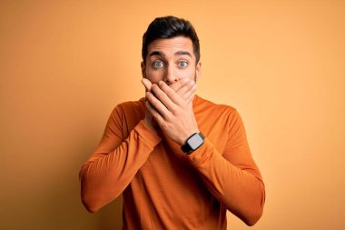 Sarı arka planda dikilen sakallı, genç ve yakışıklı bir adam yanlışlıkla ağzını kapatarak şok geçirdi. Gizli konsept.