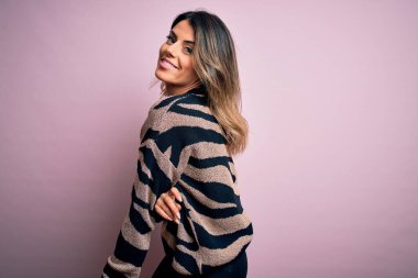 Moda kıyafetleri giyen genç ve güzel bir kadın. Manken, sokak tarzı giyiniyor. Pembe arka planda dikiliyor.