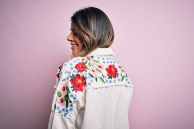 Moda kıyafetleri giyen genç ve güzel bir kadın. Manken, sokak tarzı giyiniyor. Pembe arka planda dikiliyor.