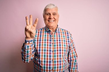 Kıdemli yakışıklı, beyaz gömlekli, pembe arka planda yalnız gezen, kendinden emin ve mutlu bir şekilde gülümseyen, üç numarayı işaret eden adam..