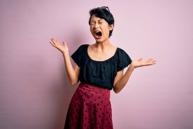 Genç ve güzel Asyalı bir kız pembe arka planda dikilip kollarını kaldırmış heyecanla haykırarak çılgın ve çılgın bir başarıyı kutluyor. Kazanan konsept