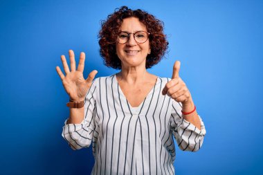 Orta yaşlı, kıvırcık saçlı, rahat çizgili tişört giyen, izole edilmiş arka planda altı numarayı gösteren ve gülümseyen, kendinden emin ve mutlu bir kadın..