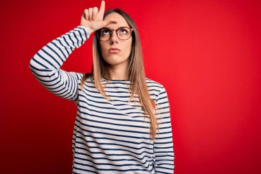 Kırmızı arka planda duran mavi gözlü genç, güzel sarışın kadın. Alnında parmakları olan insanlarla dalga geçiyor. Ezik hareketler yapıyor, alay ediyor ve hakaret ediyor..