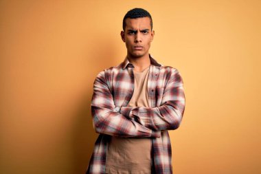 Sarı arka plan kuşkucu ve gergin, kollarını kavuşturmuş suratında tasvip etmeyen, gündelik gömlekler giyen genç, Afro-Amerikan bir adam. Negatif kişi.