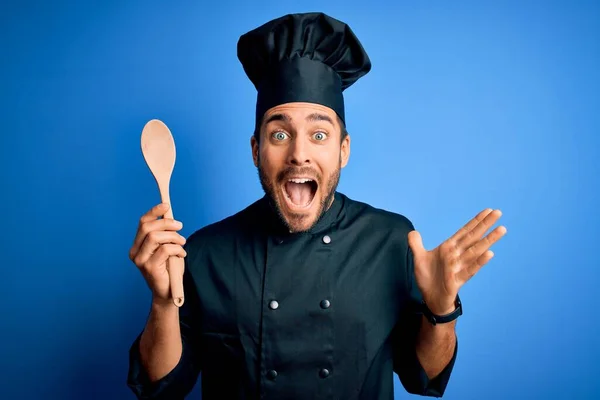 Mladý Kuchař Muž Plnovousem Uniformě Drží Dřevěnou Lžíci Modrém Pozadí — Stock fotografie