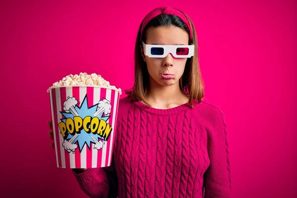 Young beautiful girl watching movie using 3d glasses eating box with popcorns depressed and worry for distress, crying angry and afraid. Sad expression.