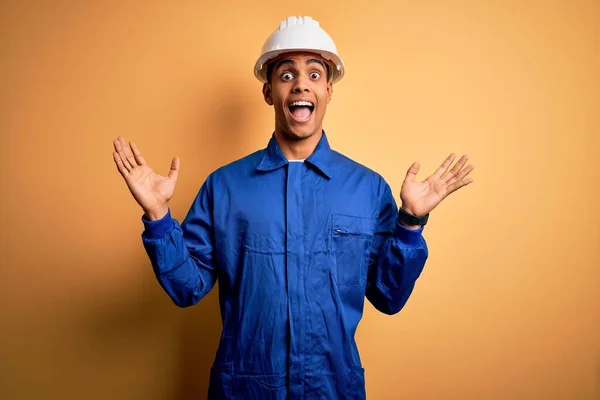 年轻英俊的非洲裔美国工人 身穿蓝色制服 头戴安全帽 兴奋地高举双臂 睁开眼睛尖叫 庆祝胜利 赢的概念 — 图库照片