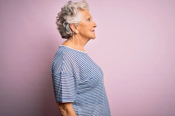 Senior beautiful grey-haired woman wearing casual t-shirt over isolated pink background looking to side, relax profile pose with natural face with confident smile.