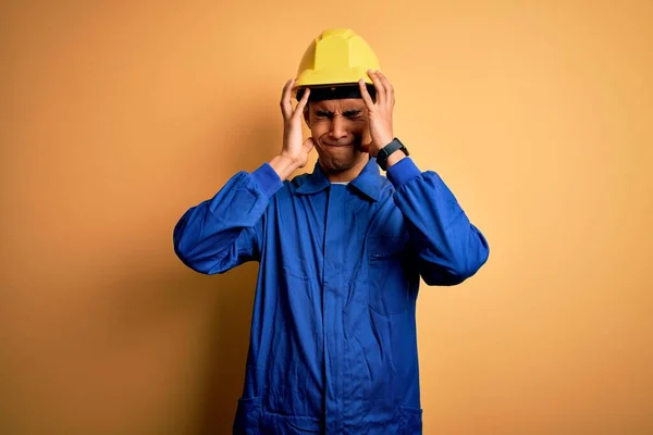 年轻英俊的非洲裔美国工人 身穿蓝色制服 头戴安全帽 因疼痛和偏头痛而陷入绝望和压力 手放在头上 — 图库照片