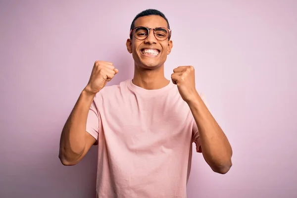 Przystojny Afroamerykanin Luźnej Koszulce Okularach Różowym Tle Podekscytowany Sukcesem Podniesionymi — Zdjęcie stockowe