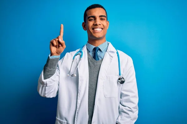 英俊的非洲裔美国医生 身穿外套和听诊器 头戴蓝色背景 带着第一指尖 面带微笑 自信而快乐 — 图库照片