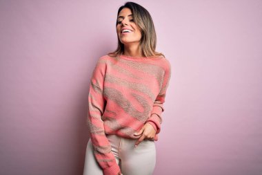 Moda kıyafetleri giyen genç ve güzel bir kadın. Manken, sokak tarzı giyiniyor. Pembe arka planda dikiliyor.