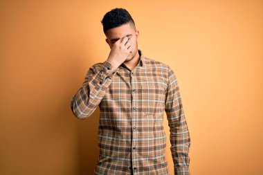 İzole edilmiş sarı arka planda dikilen sıradan tişört giyen genç yakışıklı yorgun burnu ve gözleri ovuşturarak yorgunluk ve baş ağrısı hissediyordu. Stres ve hüsran kavramı.