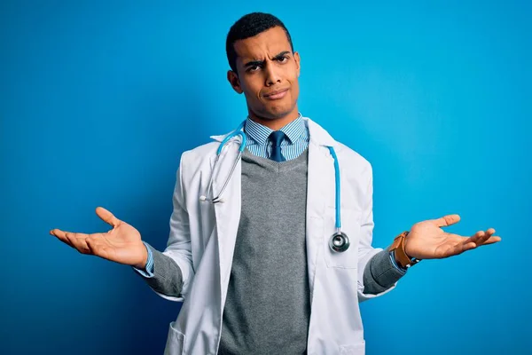英俊的非洲裔美国医生 身穿外套和听诊器 身披蓝色背景 毫无头绪 与张开双臂混淆不清 没有概念 — 图库照片