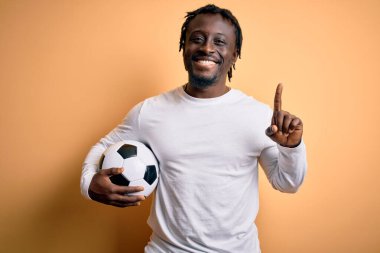 Futbol oynayan Afrikalı genç bir Amerikalı futbolcu sarı arka planda futbol topunu tutarken bir fikir ya da soru işareti ile şaşırdı.