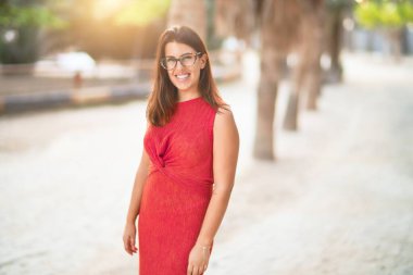 Genç ve güzel bir kız gülümseyerek mutlu ve kendinden emin bir şekilde parkta yürüyor, yüzünde bir gülümsemeyle duruyor.