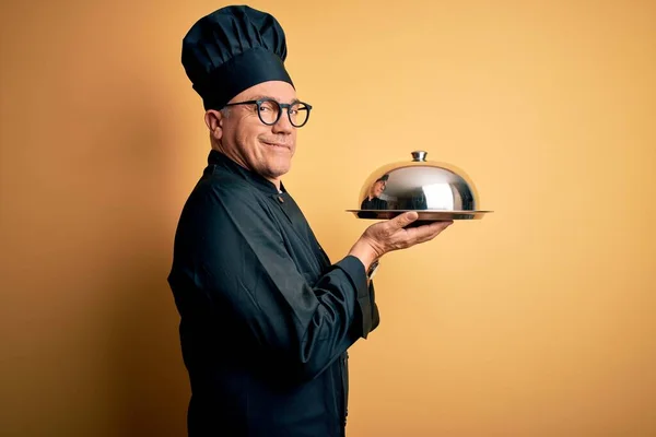 Middle age handsome grey-haired waiter man wearing cooker uniform and hat holding tray pointing aside with hands open palms showing copy space, presenting advertisement smiling excited happy