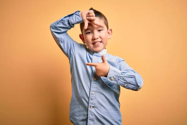 黄色の孤立した背景に立つエレガントなシャツを着ている若い男の子は 幸せな顔をした手と指でフレームを作り笑顔 創造性と写真の概念 — ストック写真