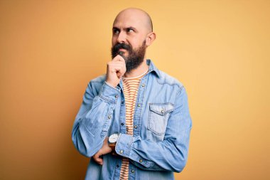 Sakallı, sıradan bir kot ceket giyen, eli çenesinde çizgili tişörtlü soru soran, düşünceli, kel bir adam. Düşünceli bir yüzle gülümsüyor. Şüphe kavramı.