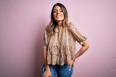 Moda kıyafetleri giyen genç ve güzel bir kadın. Manken, sokak tarzı giyiniyor. Pembe arka planda dikiliyor.