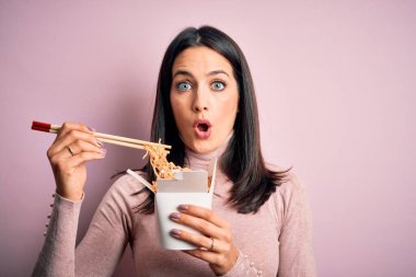 Sarı arka planda paket paket paket karton kutu taşıyan genç esmer kadın şaşırmış bir yüzle korkmuş ve korku ifadesinden heyecanlanmış.