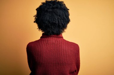 Kıvırcık saçlı, balıkçı yaka kazak giyen, kollarını kavuşturup arkaya bakan güzel Afro-Amerikan kadın.