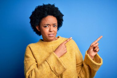 Kıvırcık saçlı, sarı kazaklı, Afro-Amerikan bir kadın. Endişeli ve gergin bir kenara işaret ediyor. Endişeli ve şaşırmış bir ifade.