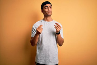 Yakışıklı Afro-Amerikan sporcusu spor giyer sarı arka plan üzerine spor giyer, elleriyle para hareketi yapar, maaş ödemesi ister, milyonerlik işi yapar.