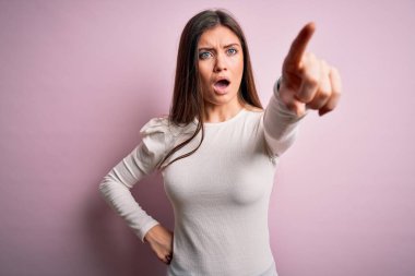 Mavi gözlü genç bir kadın pembe arkaplan üzerine gündelik beyaz tişört giyiyor. Parmağıyla işaret ediyor. İleride şaşırmış, ağzı açık, ön tarafta bir şey var.