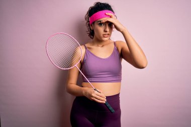 Kıvırcık saçlı, spor giyinen, badminton oynayan güzel bir sporcu kadın. Kafa kafaya raket oynuyor. Utanç ve şaşkınlık dolu bir yüz ifadesi var. Hata için korku ve üzüntü.