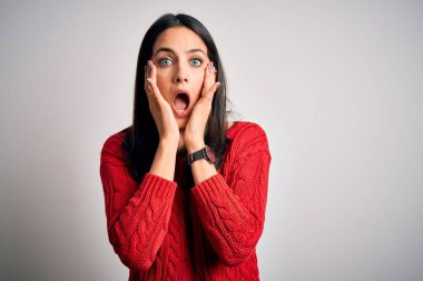 Young brunette woman with blue eyes wearing casual sweater over isolated white background afraid and shocked, surprise and amazed expression with hands on face