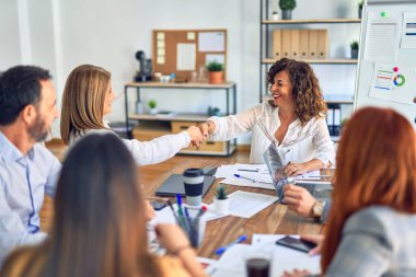 Bir grup iş adamı mutlu ve kendinden emin gülümsüyor. Birlikte çalışırken gülümseyerek ofiste el sıkışırken.