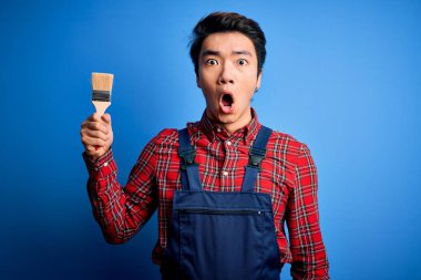 Önlük giyen genç, yakışıklı Çinli ressam. Fırça kullanıyor. Şaşırmış bir yüz ifadesinden korkuyor ve heyecanlanıyor.