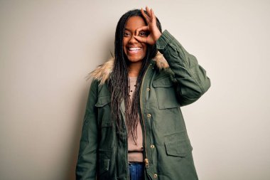 Genç Afrikalı Amerikalı kadın, izole edilmiş arka planda kışlık parka ceket giyiyor. El hareketleriyle gülümsüyor, gözleriyle mutlu yüzlere bakıyor..
