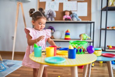 Anaokulunun masasında çatal bıçak ve yemek oyuncaklarıyla oynayan genç ve güzel bir çocuk.