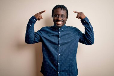 Genç, yakışıklı, Afro-Amerikalı bir adam beyaz arka plan üzerinde dikilmiş gülümsüyor, iki eliyle başını işaret ediyor, harika bir fikir ya da düşünce, iyi bir hafıza.