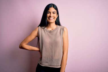 Moda kıyafetleri giyen genç ve güzel bir kadın. Manken, sokak tarzı giyiniyor. Pembe arka planda dikiliyor.