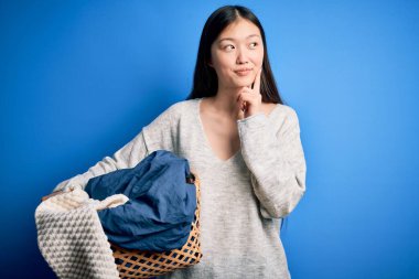 Hasır çamaşır sepetini tutan genç Asyalı kadın ev işleri yapıyor. Ciddi yüz ifadeleri takınıyor.