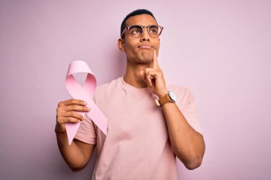 Genç, yakışıklı, Afro-Amerikan bir adam pembe kanser kurdelesini soyutlanmış arka planda saklıyor.