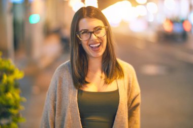 Mutlu ve kendinden emin gülümseyen genç ve güzel bir kadın. Kasaba caddesinde yüzünde gülümsemeyle dikilirken