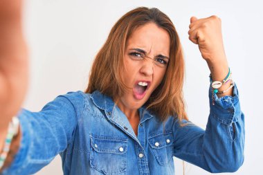 Genç kızıl saçlı kadın izole bir arka planda selfie çekiyor. Sinirli ve sinirli bir şekilde bağırıyor, çıldırıyor ve el kaldırarak bağırıyor. Öfke kavramı.