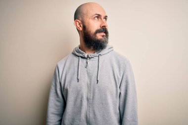 Sakallı, yakışıklı, kel bir adam pembe arka planda dikilip yüzünde gülümseme, doğal bir ifade ile yan yana bakıyor. Kendinden emin gülen.