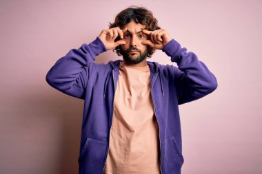 Genç, yakışıklı, sakallı, pembe arka planda rahat bir kazak giyen, gözlerini parmaklarıyla açmaya çalışan, uykulu ve yorgun bir adam.