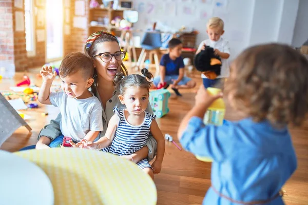 Beautiful teacher and group of toddlers playing around lots of toys at kindergarten