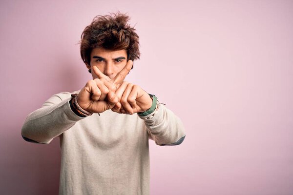 Young handsome man wearing casual t-shirt standing over isolated pink background Rejection expression crossing fingers doing negative sign