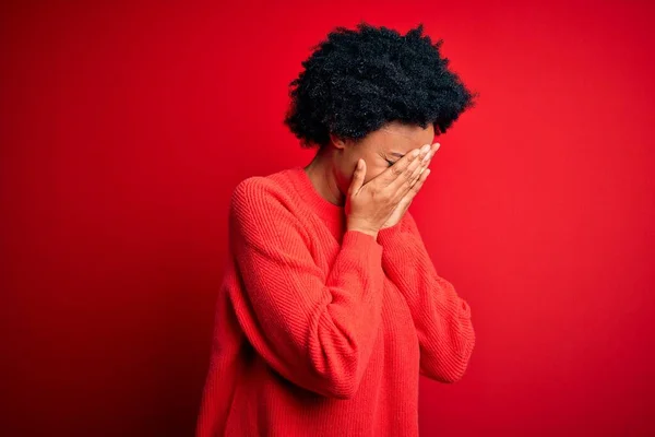 Young beautiful African American afro woman with curly hair wearing casual sweater with sad expression covering face with hands while crying. Depression concept.